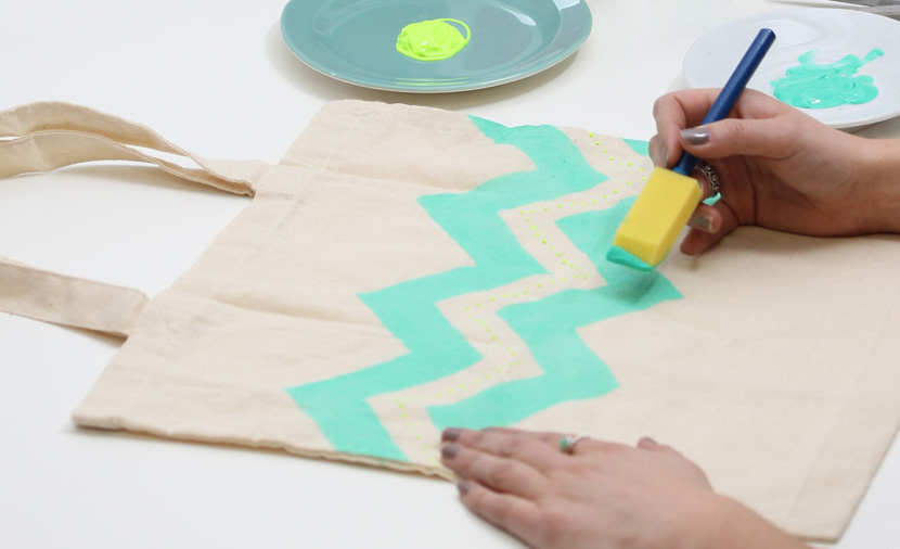 Dieťa maľuje na textil pomocou tyrkysovej farby a tupovacieho štetca.